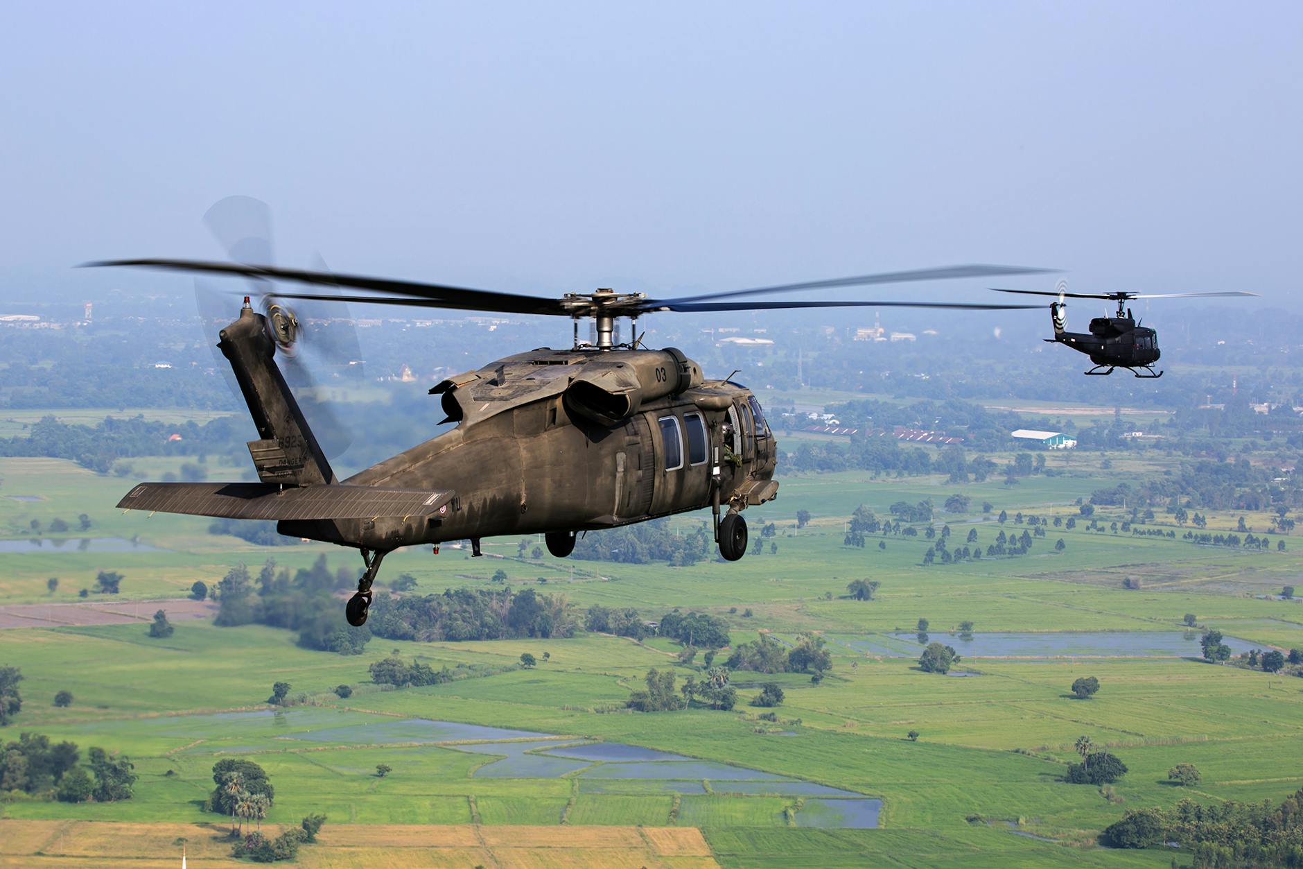 brown helicopter flying above green field during daytime
