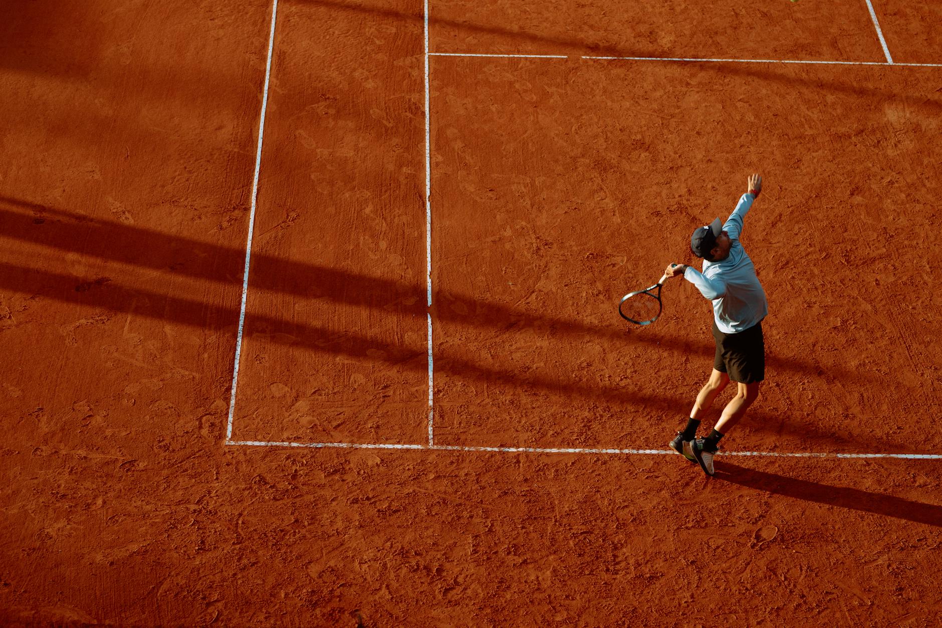 tennis player serving on clay court at sunset